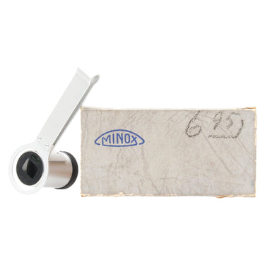 Minox film viewer with folding clip raised and lens facing forward, next to original Minox-marked box