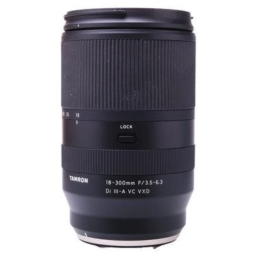 Tamron 18-300mm Di III-A VC VXD lens standing upright with front cap and hood on top, zoom ring and LOCK switch